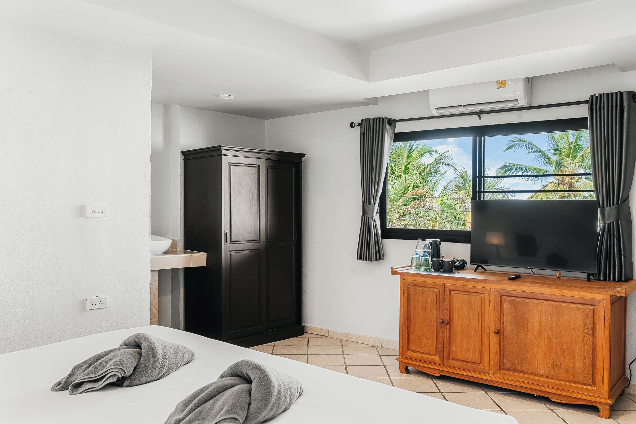 A hotel room with a bed, a wooden cabinet, a television, and a window with curtains.