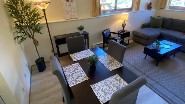 Et spiseområde med et bord dækket til fire personer, en sofa og en lampe.