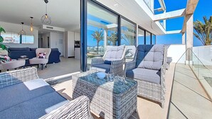 A modern living room with a large glass wall, wicker furniture, and a view of the city. - Bright Apartment with Expansive Poolside Balcony (Mar de Cristal)