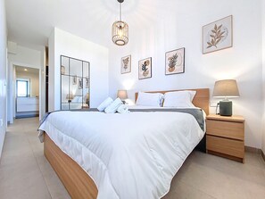 A modern bedroom with a large bed, bedside tables, a mirror, and wall art. - Bright Apartment with Expansive Poolside Balcony (Mar de Cristal)