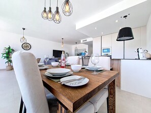 A modern dining area with a wooden table set for four, surrounded by white upholstered chairs. - Bright Apartment with Expansive Poolside Balcony (Mar de Cristal)