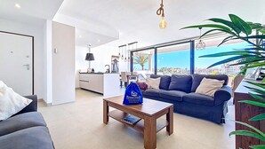 A modern living room with a sofa, a coffee table, and a view of the city. - Bright Apartment with Expansive Poolside Balcony (Mar de Cristal)
