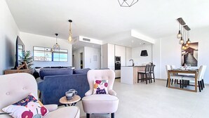 A modern living room with a sofa, armchairs, a coffee table, and a dining area with a table and chairs. - Bright Apartment with Expansive Poolside Balcony (Mar de Cristal)
