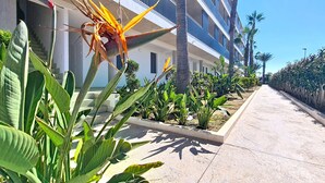 A hotel corridor with a modern design, featuring a concrete floor and a row of balconies with palm trees. - Bright Apartment with Expansive Poolside Balcony (Mar de Cristal)