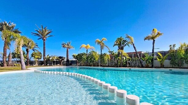 A clear blue pool with a tiled edge, surrounded by palm trees and a fence. - Bright Apartment with Expansive Poolside Balcony (Mar de Cristal)