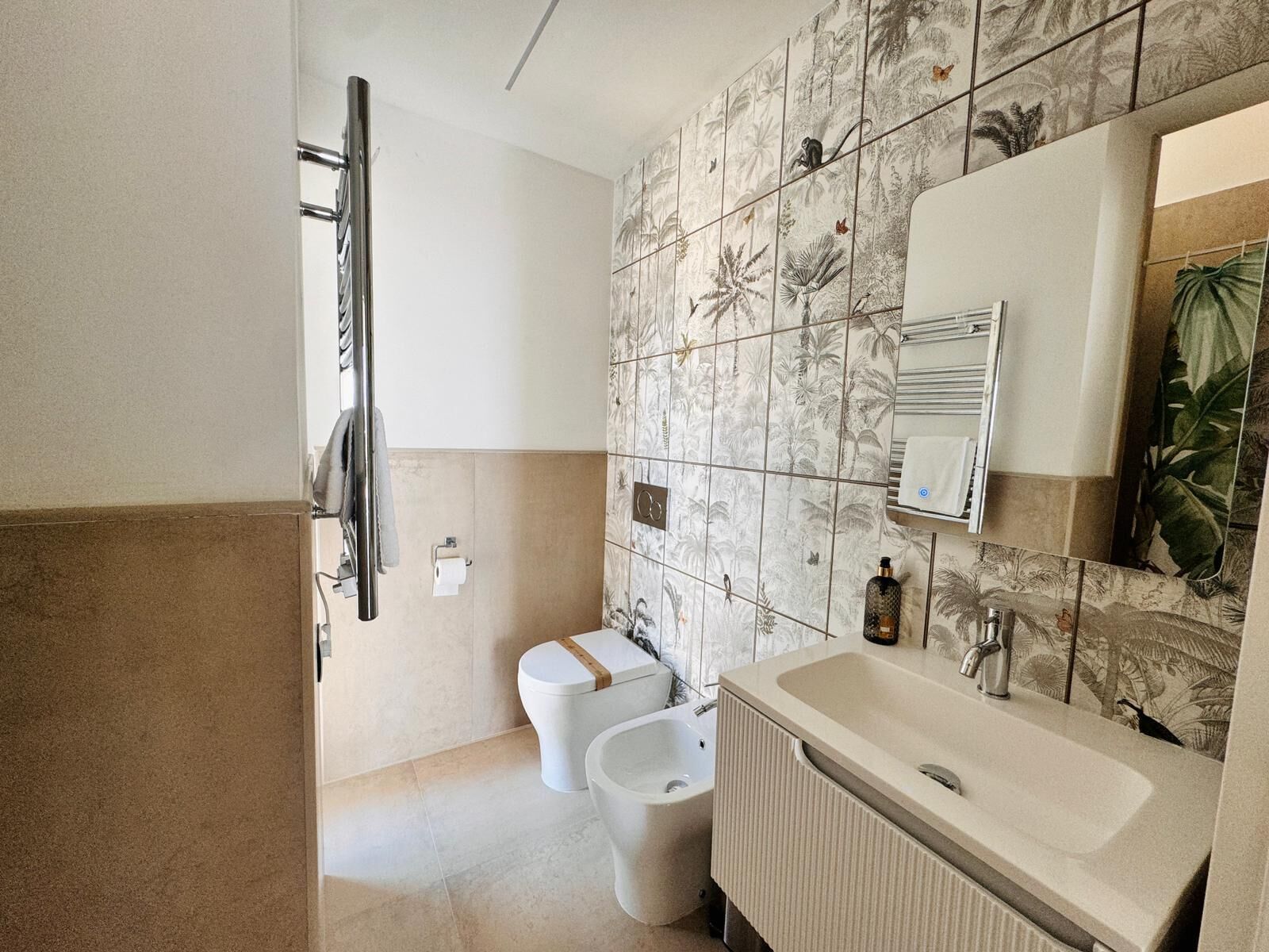 Une salle de bain comprenant des toilettes, un bidet et un lavabo, ainsi qu’un porte-serviettes et un miroir.