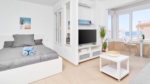A modern hotel room with a bed, TV, seating area, and a view of the sea. - Apartment 'Studio Carabela' with Sea View, Wi-Fi and Air Conditioning (Torrox)