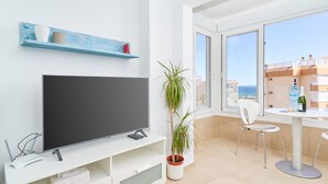 A modern living room with a flat-screen TV, a potted plant, a dining table with chairs, and a large window with a view of the sea. - Apartment 'Studio Carabela' with Sea View, Wi-Fi and Air Conditioning (Torrox)