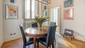 Et spiseområde med et træbord, sorte stole, en vase med blomster og billedkunst på væggene.