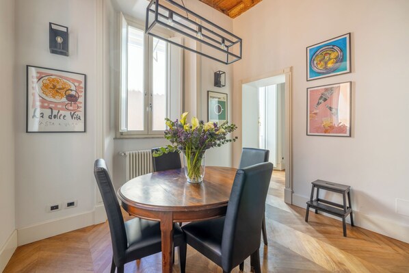 Un coin repas avec une table en bois, des chaises noires, un vase de fleurs et des œuvres d’art accrochées aux murs.