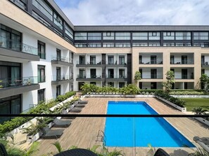 Ein modernes Gebäude mit Pool auf dem Dach, mehreren Balkonen und üppiger Bepflanzung.