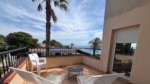 Een balkon met twee witte stoelen, een klein rond tafeltje en uitzicht op zee.