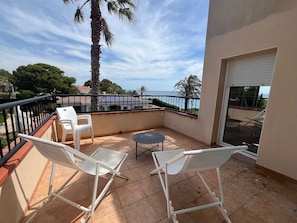 Un balcon avec deux chaises blanches, une petite table ronde et une vue sur la mer.