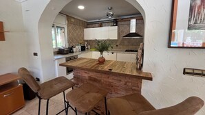 Een keuken met een centraal eiland, barkrukken, een potplant en een ingelijst foto aan de muur.