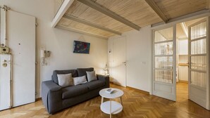 Una habitación con suelo de madera estampada en espiga, un sofá gris con cojines, una mesita blanca y un cuadro en la pared.
