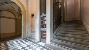 Un pasillo con piso a cuadros, una escalera con barandilla de metal y una puerta con celosía decorativa.