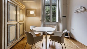 Un comedor con una mesa redonda y cuatro sillas, un radiador, una ventana con cortinas y un mueble con molduras decorativas.
