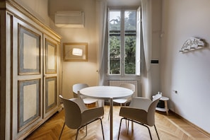 Un coin repas comprenant une table ronde et quatre chaises, un radiateur, une fenêtre avec des rideaux et un meuble agrémenté de moulures décoratives.