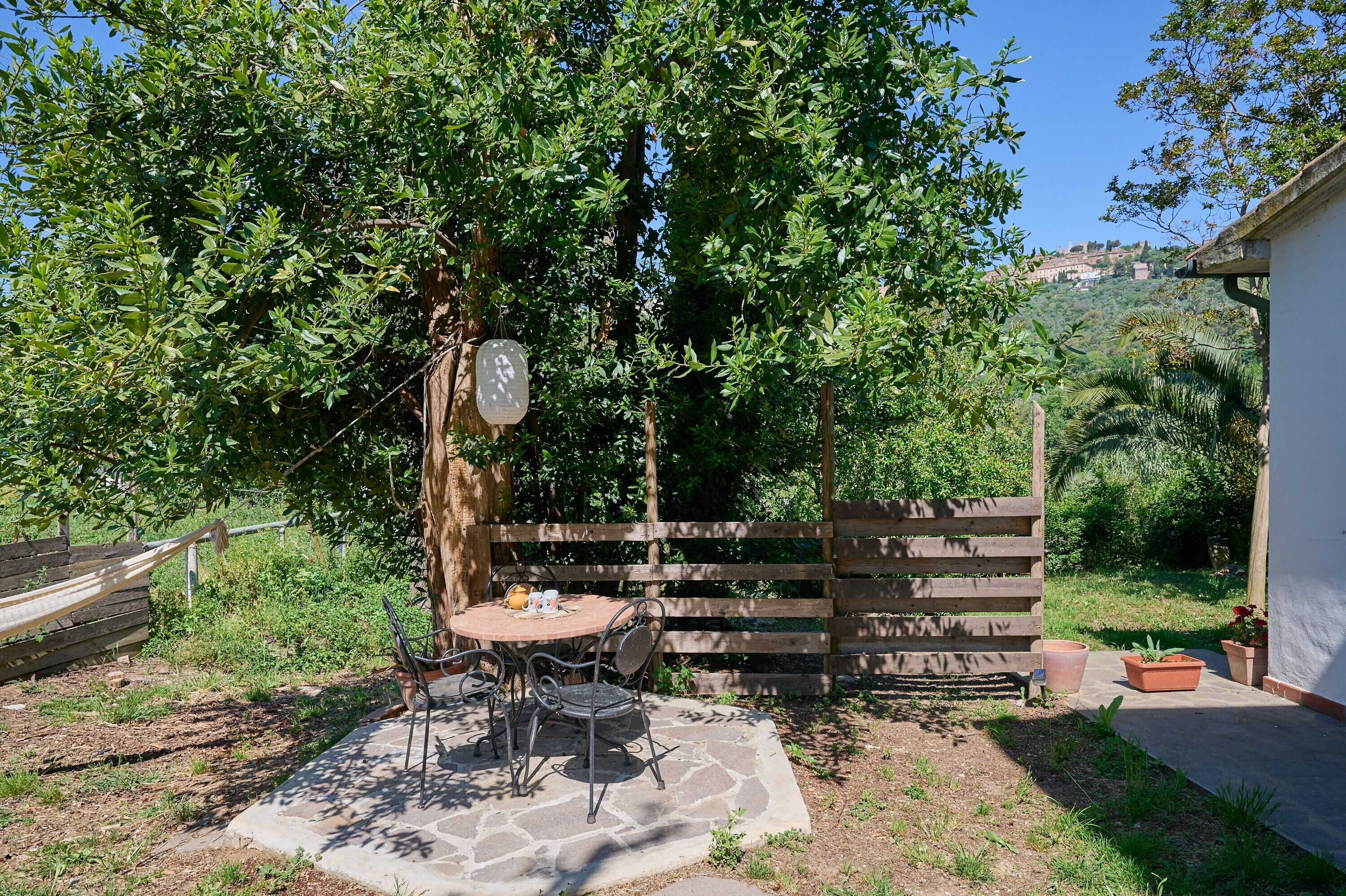 Un patio con mesa y sillas, rodeado por una cerca de madera y abundante vegetación.