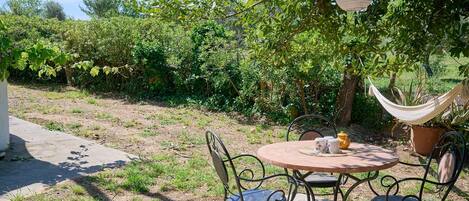 A patio with a round table and metal chairs, surrounded by greenery and a hammock.