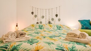 A bed with a floral bedspread, a wall-mounted decoration, and two rolled towels. - Room 'Camera D'ambra' with Private Terrace, Private Garden and Wi-Fi (Campiglia Marittima)