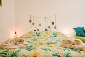 Ein Bett mit floraler Bettdecke, eine Wanddekoration und zwei gerollte Handtücher.