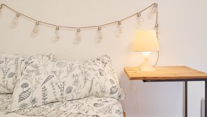 A bed with patterned bedding, a bedside table with a lamp, and a string of light bulbs on the wall. - 'La Stanza di Campagna' with Shared Garden and Wi-Fi (Campiglia Marittima)