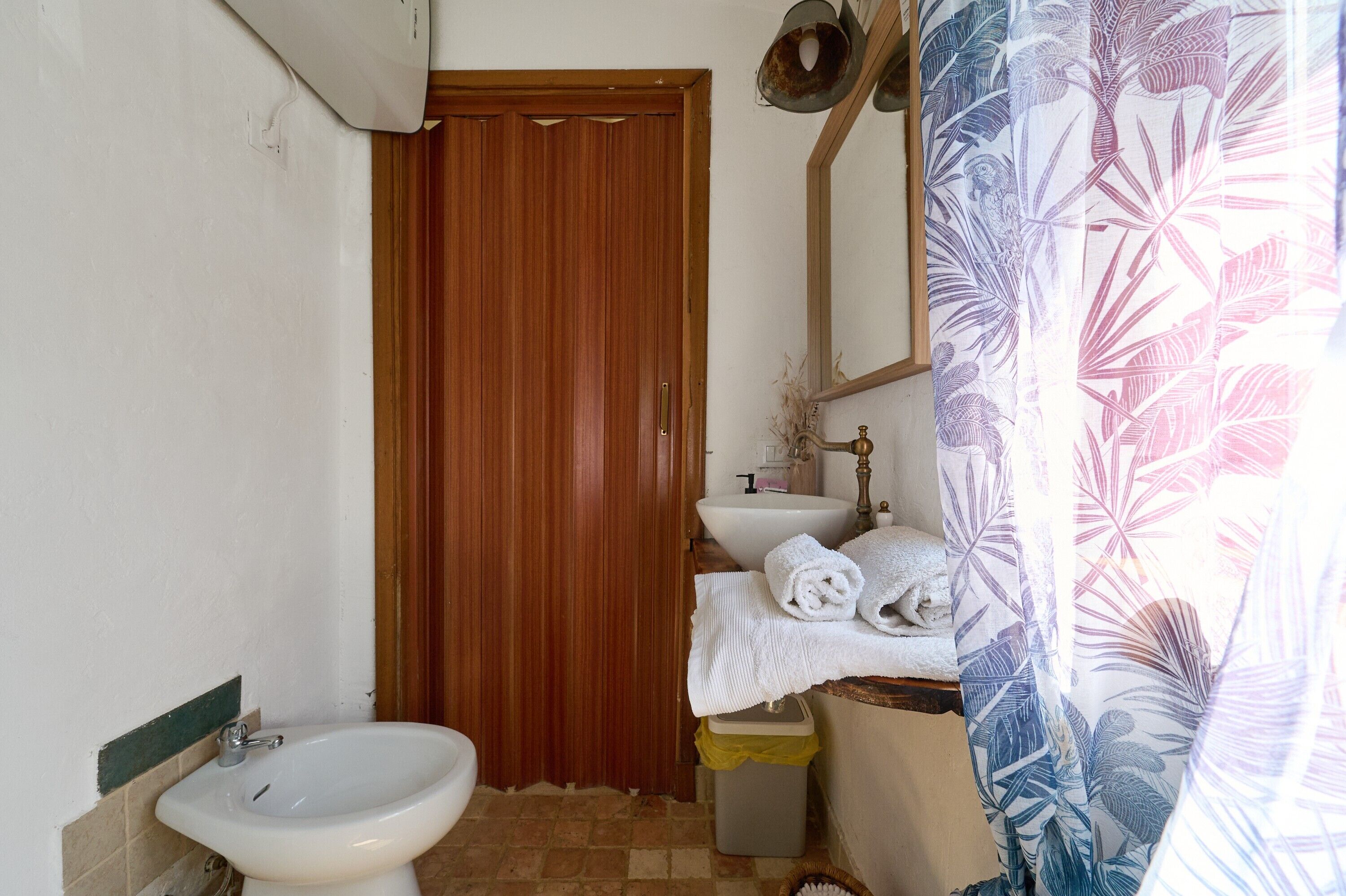 Ein Badezimmer mit Holztür, Waschbecken, Bidet und einer Duschvorhang mit Blättermotiv.