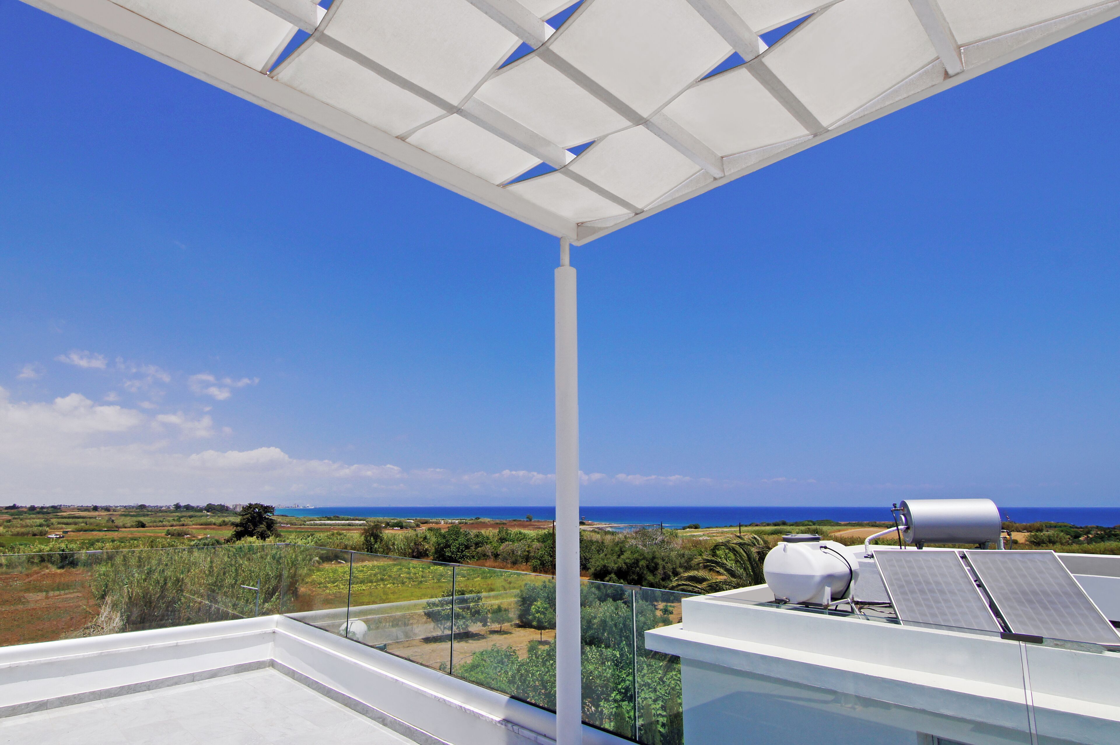 Eine Dachterrasse mit Solaranlage, einer weißen Pergola und Blick auf das Meer und die Landschaft.