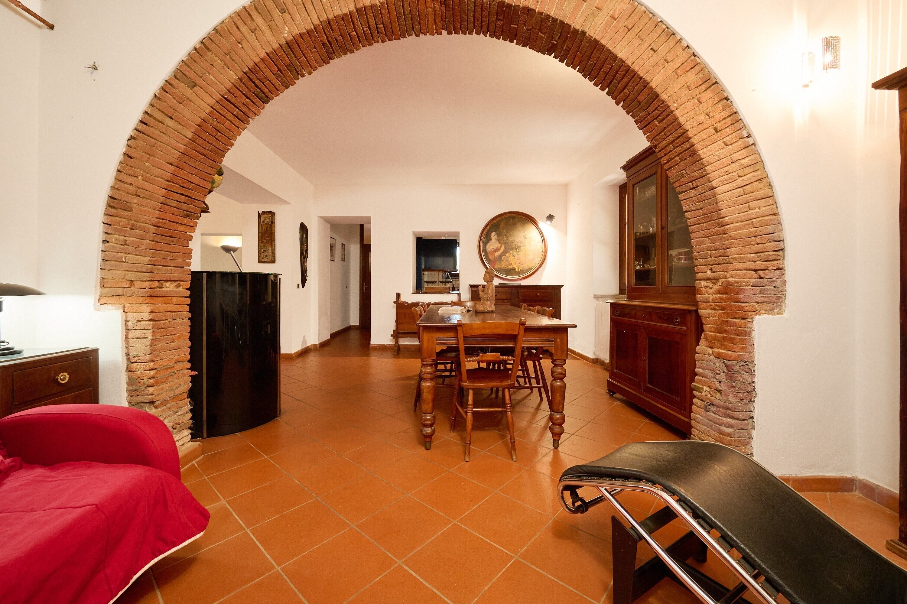 Una stanza con un arco in mattoni, un tavolo da pranzo con sedie, un divano rosso e una sedia nera.