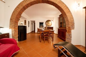 Ein Zimmer mit einer Ziegelbogenarchitektur, einem Esstisch mit Stühlen, einem roten Sofa und einem schwarzen Sessel.
