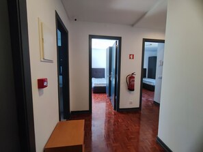 A hallway with a wooden floor, a fire extinguisher, and a red emergency box.