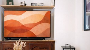 Ett vardagsrum med en tv-apparat placerad på ett träskåp, ett runt träbord med en vas och ett litet svart bord med en lampa.