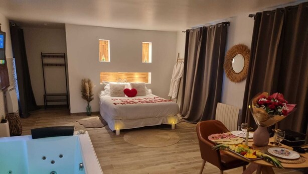 A modern hotel room with a large bed, a sitting area with a table set for two, and a bathtub with a lotus-shaped candle. - Luxury suite with private Jacuzzi and garden 20 minutes from Paris NetFlix (Saint-Prix)