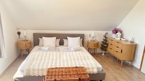 Un dormitorio con cama, dos mesitas de noche, cómoda, cesta de mimbre y una planta pequeña.