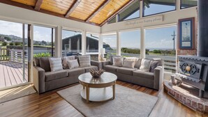 A spacious living room with a large window overlooking a deck and a scenic view. - Irish Beach | Ocean Views, Hot-tub, Beach Access (Manchester)