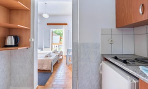 A modern kitchen with a built-in stove, a coffee maker on a shelf, and a view into a bedroom with a bed and a window. - Studio Apartment 'Maltas 6' with Shared Terrace, Wi-Fi and Air Conditioning (Corfu)