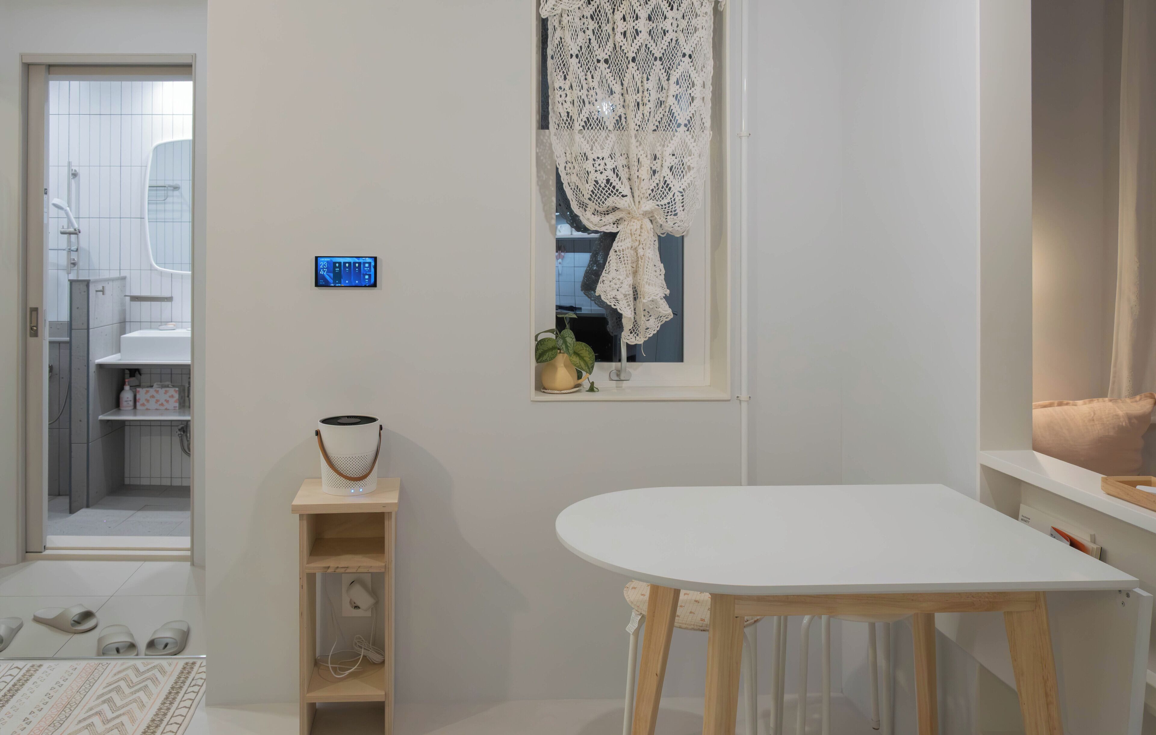 A modern bathroom with a toilet, sink, and shower. There is a small table with a basket and a potted plant. A white table is in the foreground.
