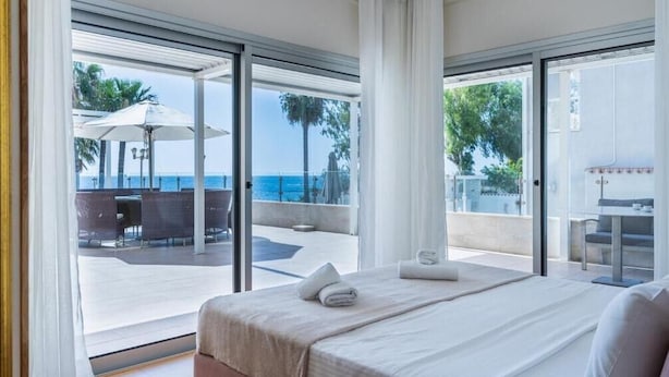 Ein Hotelzimmer mit Bett, Meerblick und einer Sitzgelegenheit im Freien mit Sonnenschirmen.