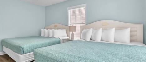 A bedroom with two beds, a ceiling fan, a window with blinds, and a bedside table with a lamp.