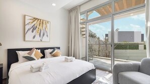 Een moderne slaapkamer met een groot bed, een grijze bank en een groot raam met uitzicht.