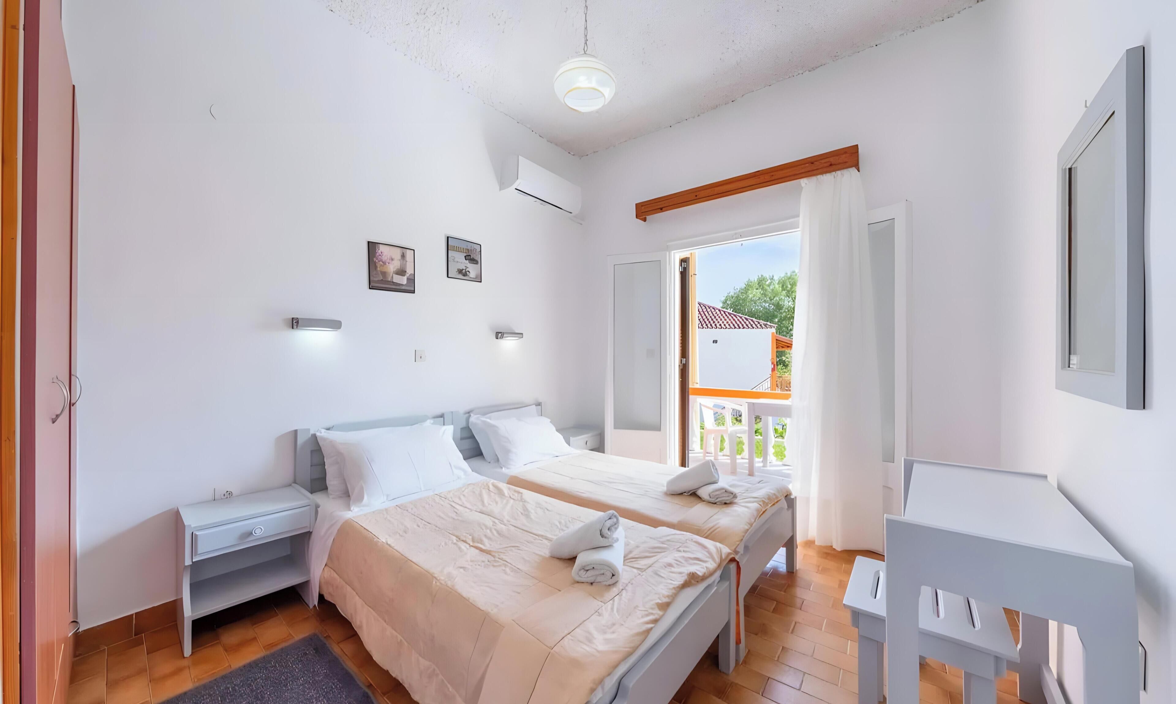 Une chambre avec deux lits, un bureau, une chaise et un balcon avec vue.