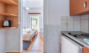 A modern kitchen with a built-in stove, a coffee maker on a shelf, and a view into a bedroom with a bed and a window. - Studio Apartment 'Maltas 6' with Shared Terrace, Wi-Fi and Air Conditioning (Corfu)