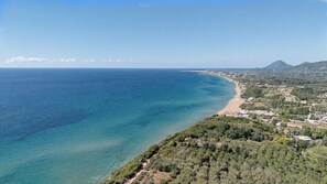 Eine Küstenlandschaft mit freiem Blick auf das Meer, einem Sandstrand und einer dicht bewachsenen Gegend mit Gebäuden.