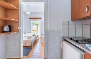 A modern kitchen with a built-in stove, a coffee maker on a shelf, and a view into a bedroom with a bed and a window. - Studio Apartment 'Maltas 6' with Shared Terrace, Wi-Fi and Air Conditioning (Corfu)