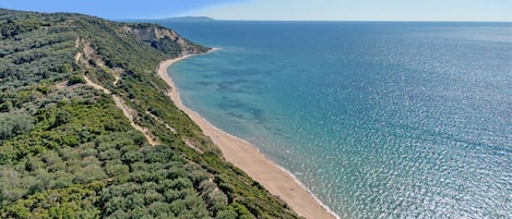 A coastal landscape with a beach, dense greenery, and a clear view of the sea.