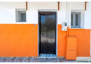 A building with a black door, orange walls, and a small window. - Studio Apartment 'Maltas 6' with Shared Terrace, Wi-Fi and Air Conditioning (Corfu)