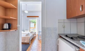 A modern kitchen with a built-in stove, a coffee maker on a shelf, and a view into a bedroom with a bed and a window. - Studio Apartment 'Maltas 6' with Shared Terrace, Wi-Fi and Air Conditioning (Corfu)