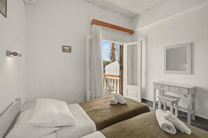Ein Hotelzimmer mit zwei Betten, einem kleinen Tisch, einem Spiegel und einem Balkon mit Blick ins Freie.