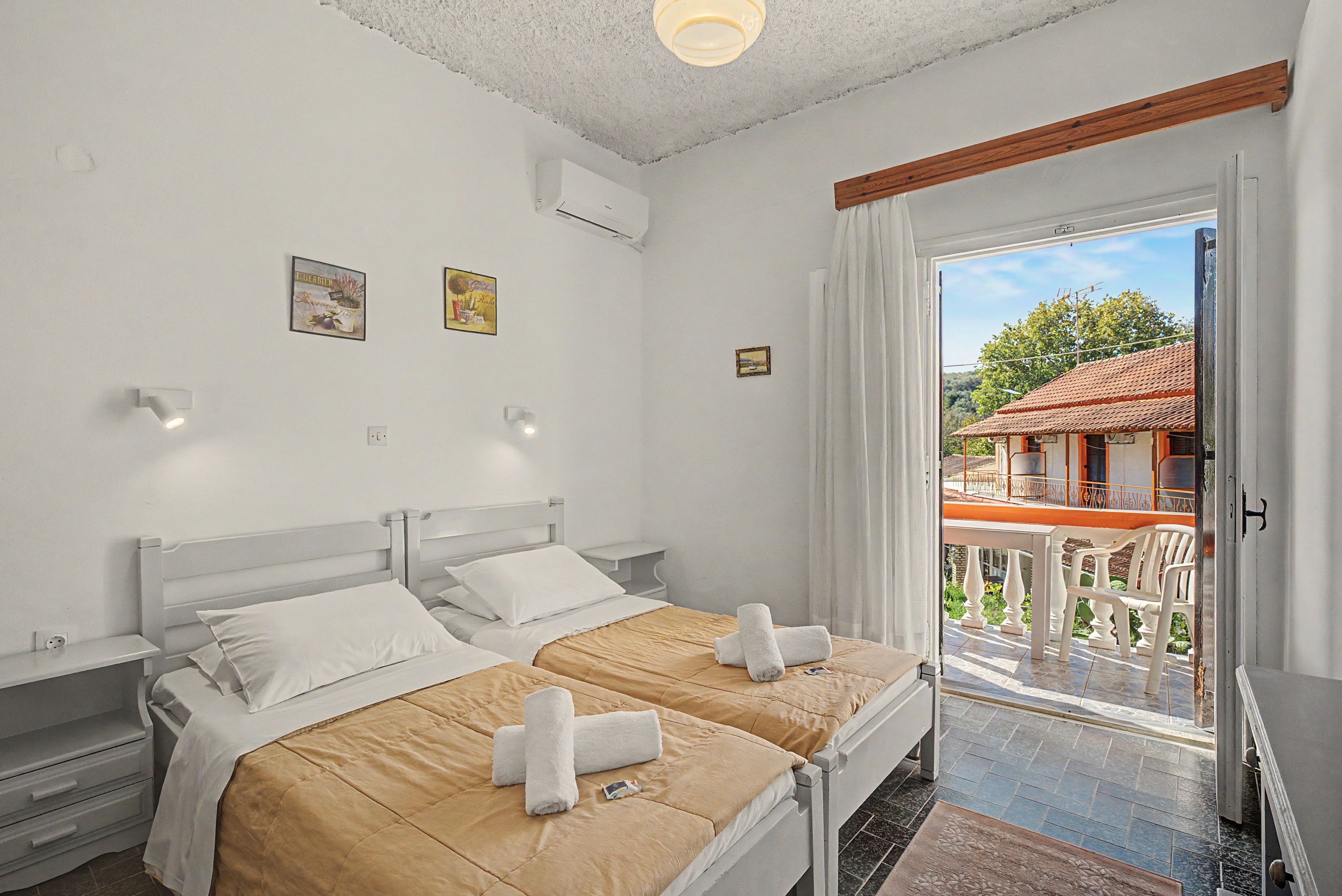 Habitación de hotel con dos camas, un balcón con vistas a un edificio y una puerta que da al exterior.